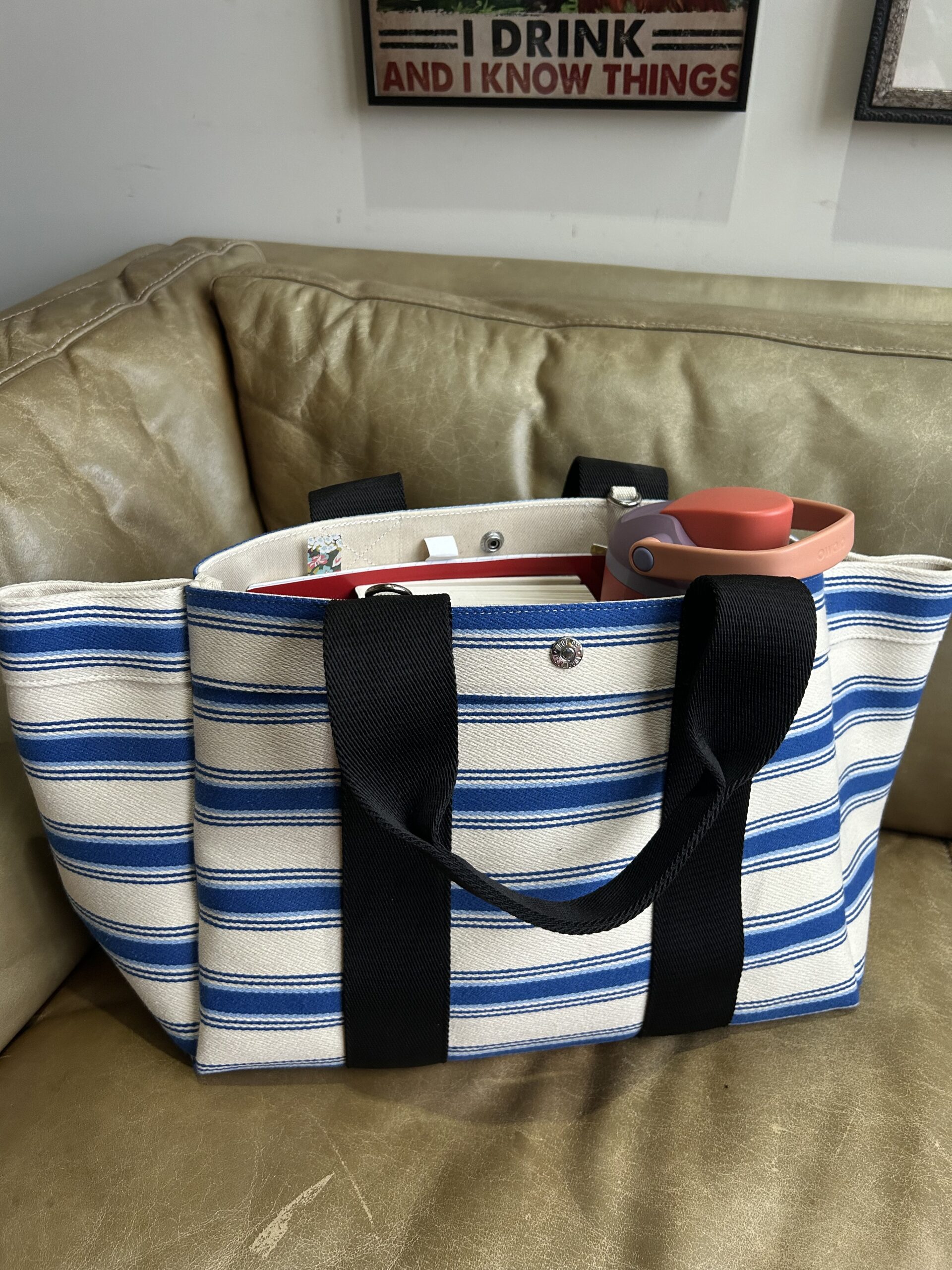 A striped canvas bag from which we can see the top of a notebook and a waterbottle.